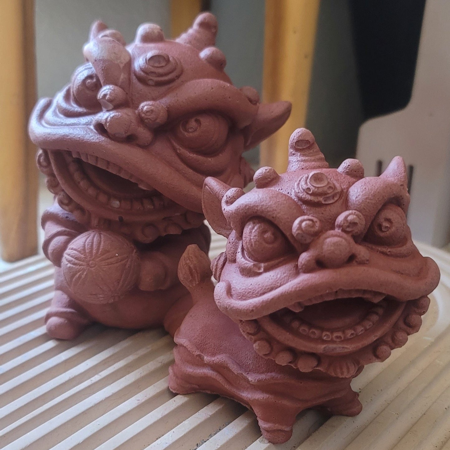 A front-facing view of a lion statue holding a ball in its paw, paired with its twin, a standing lion statue. Both are intricately detailed and set side by side, showcasing their complementary designs.