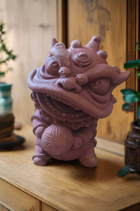 A majestic red lion statue with intricate details, holding a ball in its paw, set against a warm wooden background with Asian-inspired patterns.