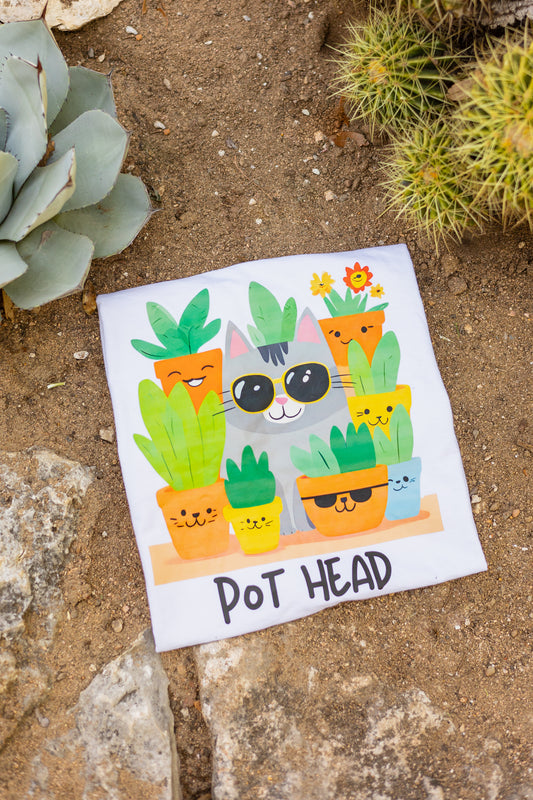 White Pot Head T-shirt flatlay with a quirky cat wearing sunglasses surrounded by plant pots, placed on a desert background surrounded by agave plants, spikey cactus, and rocks.