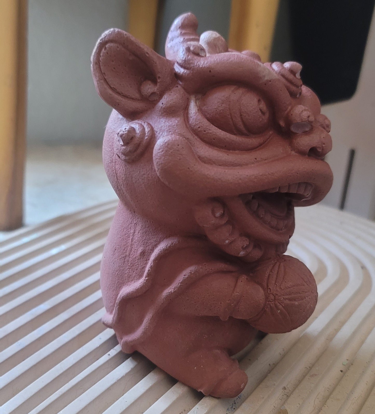 A side view of a lion statue holding a ball in its paw, highlighting its detailed design and cute, curled tail, set against the backdrop of a modern house with clean lines and minimalist decor.