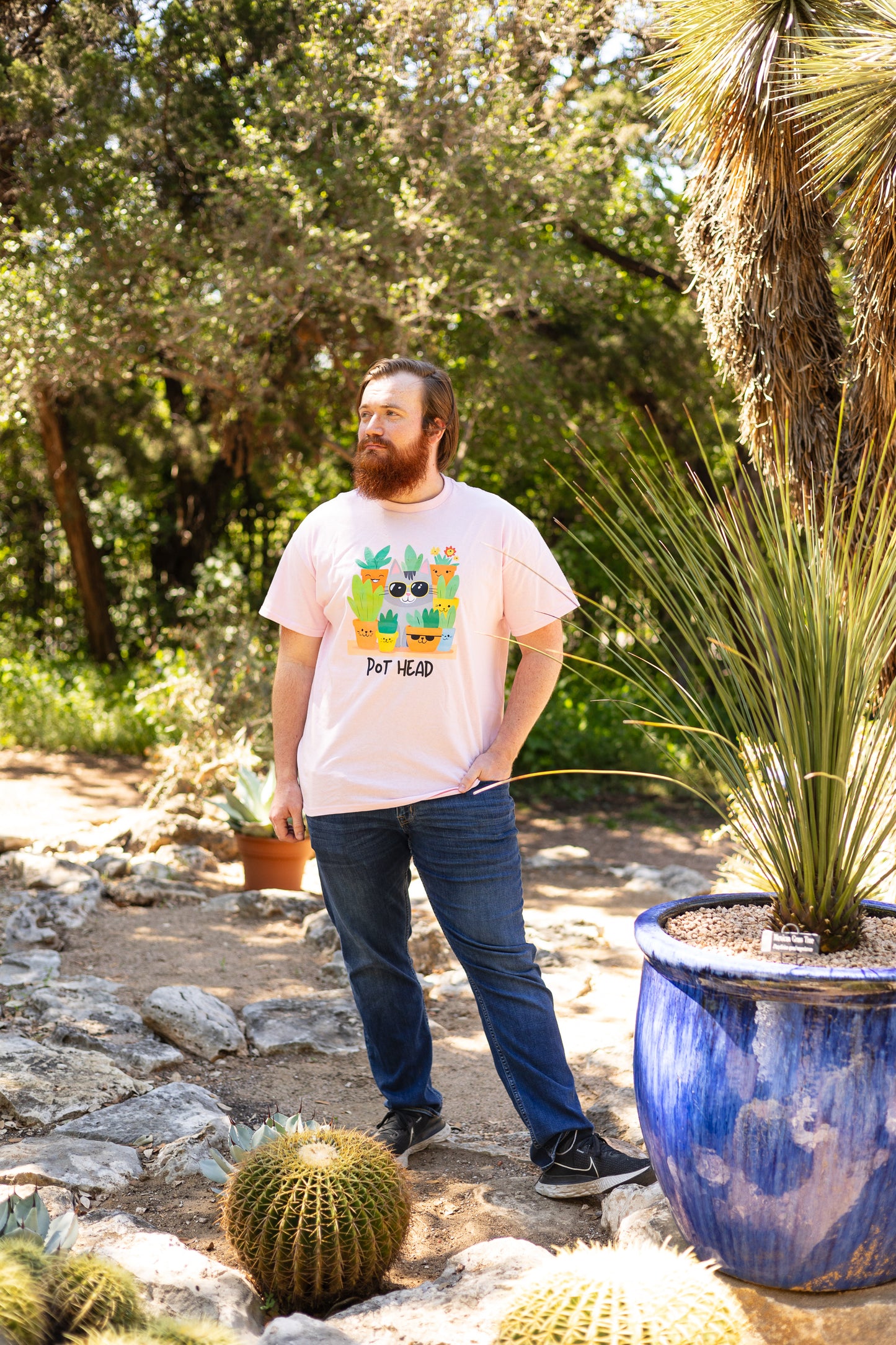 Man with a ginger beard posing in a pink Pot Head T-shirt in a desert background with a spiky cactus and a palm in a big blue pot.